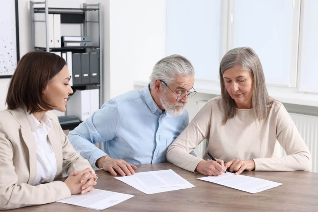 Elderly couple consulting lawyer about will at wooden table indoors